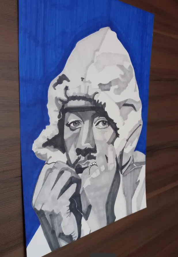 Desenho em marcador cinza sobre papel de uma pessoa de capuz claro com a mão no queixo e um anel no dedo, olhando pra frente, com o fundo pintado de azul, apoiado numa superfície de madeira