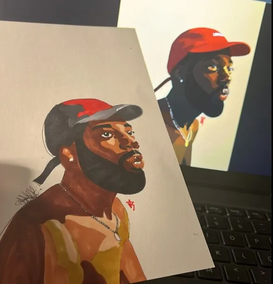O desenho do Brent Faiyaz em papel, à frente da tela de um notebook que mostra a foto de referência: ele de boné vermelho, olhando para o lado